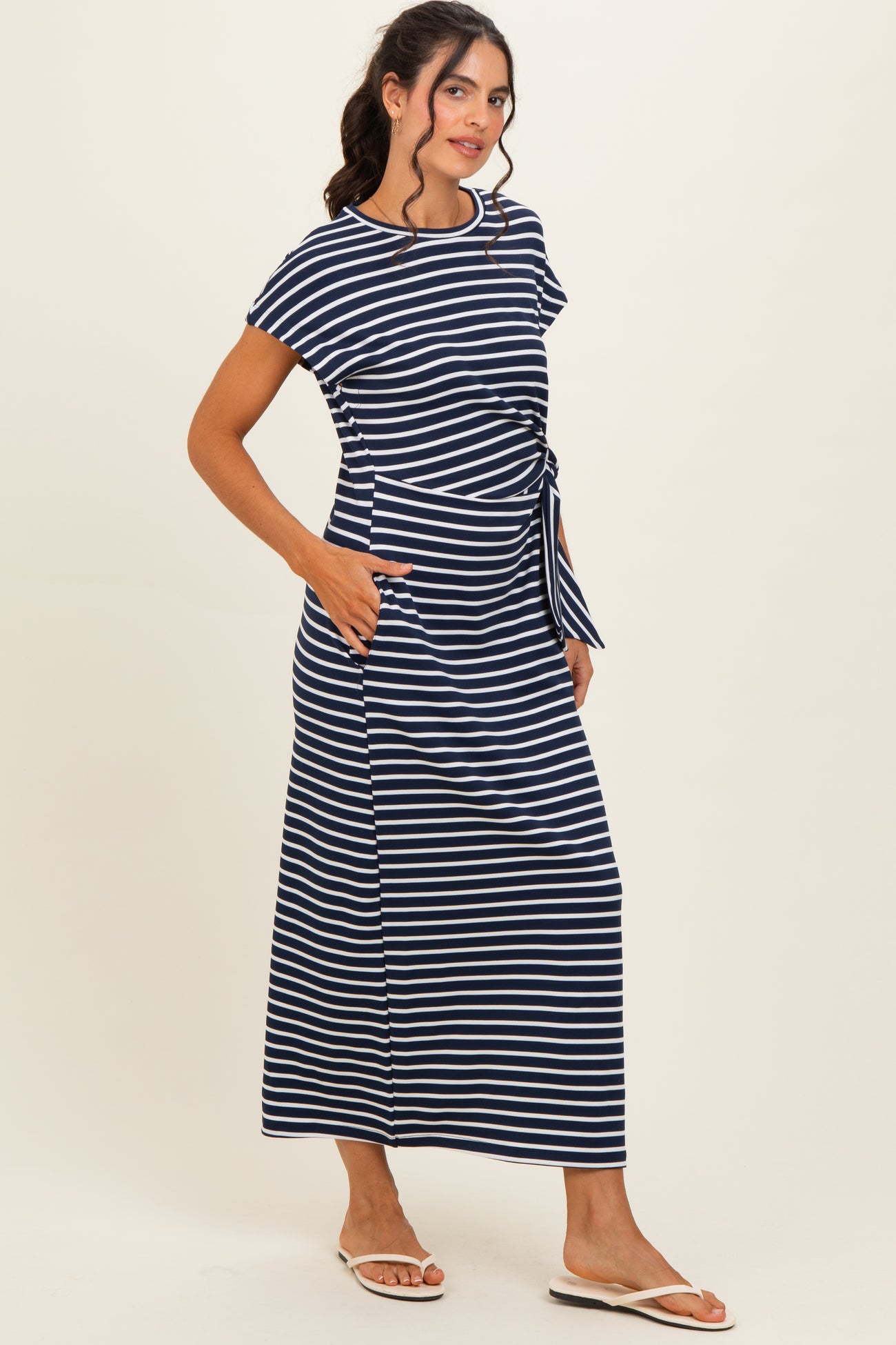 woman wearing a navy and white striped maxi dress with short sleeves and a tie detail at the waist, standing with pockets