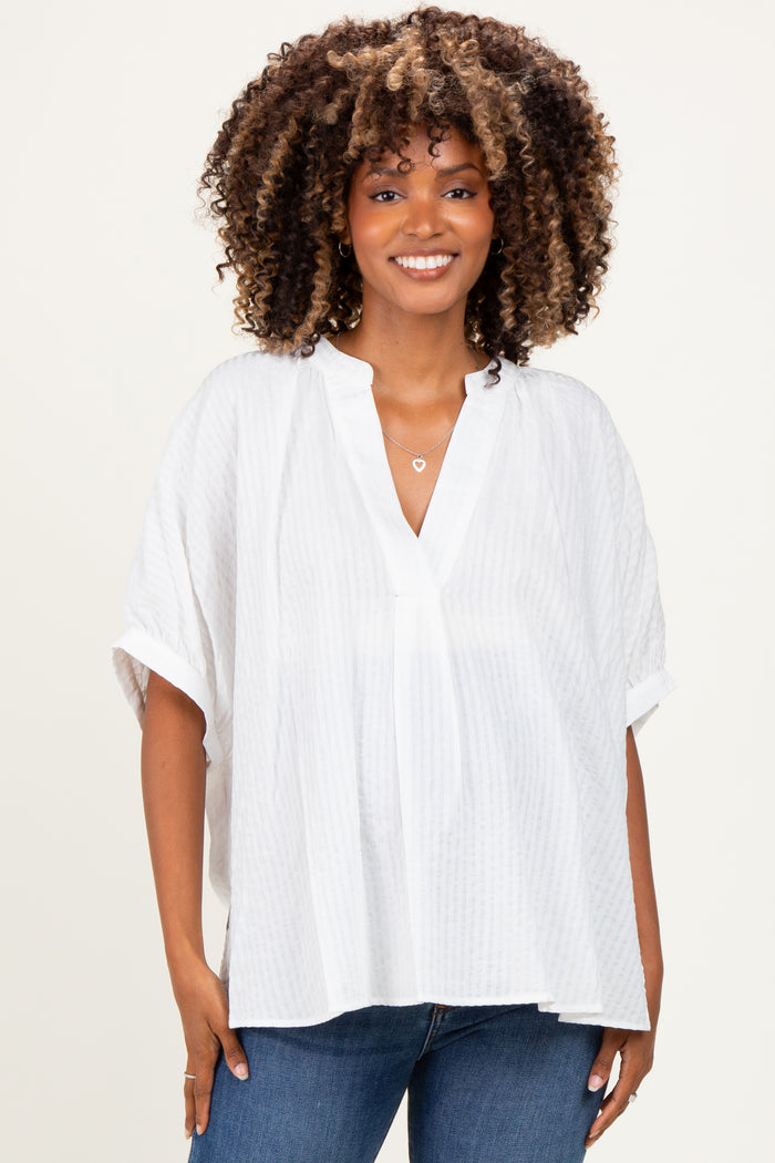 woman wearing a white oversized maternity top with a v-neck and short sleeves, smiling at the camera