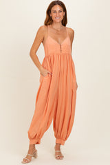 woman wearing a coral spaghetti strap jumpsuit with a button front and side pockets