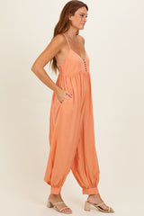 woman wearing a peach sleeveless jumpsuit with buttons and pockets, styled with beige sandals