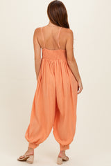 woman wearing an orange smocked-back jumpsuit with wide leg and spaghetti straps, viewed from the back