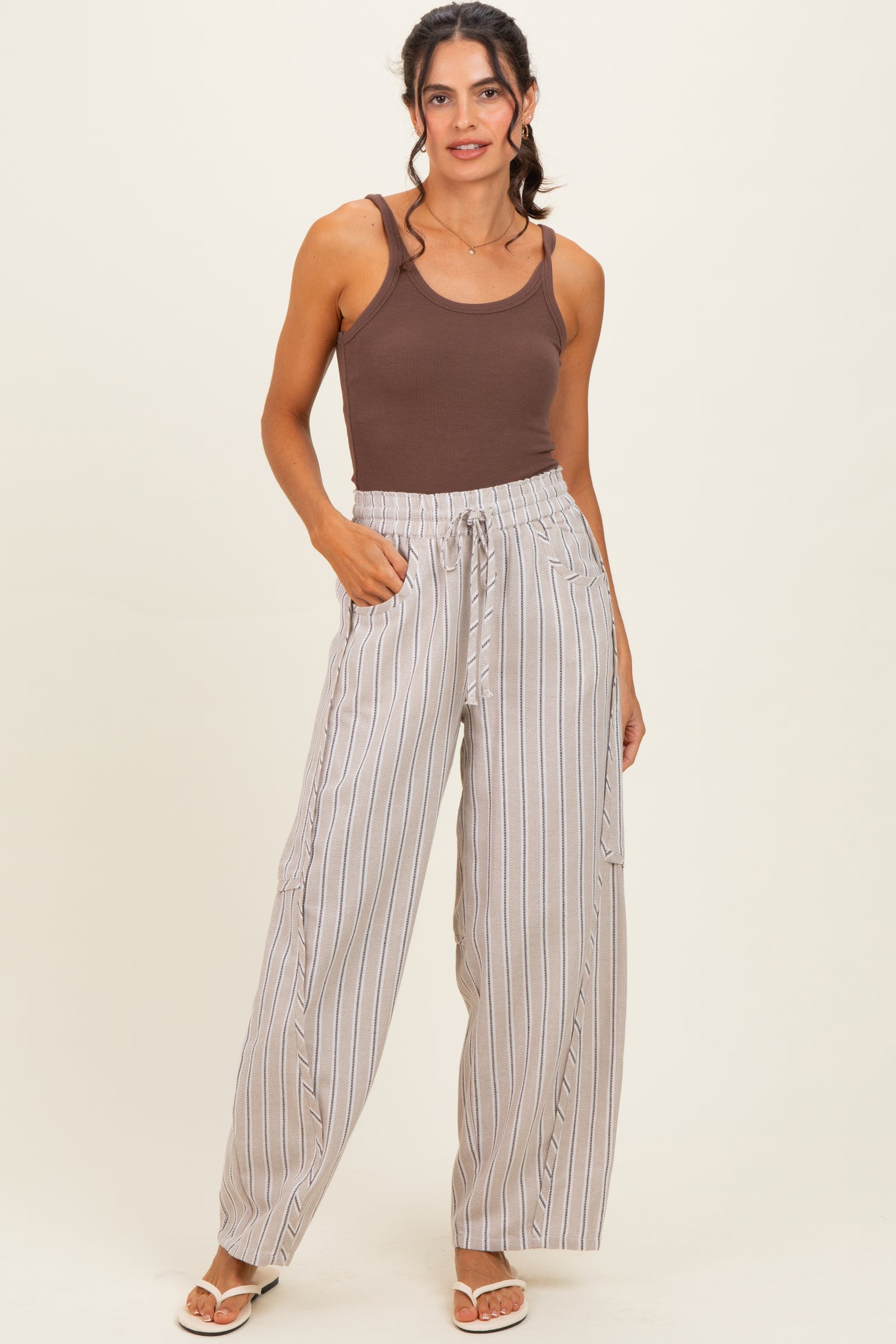 woman wearing a brown tank top and light striped wide-leg pants with side pockets