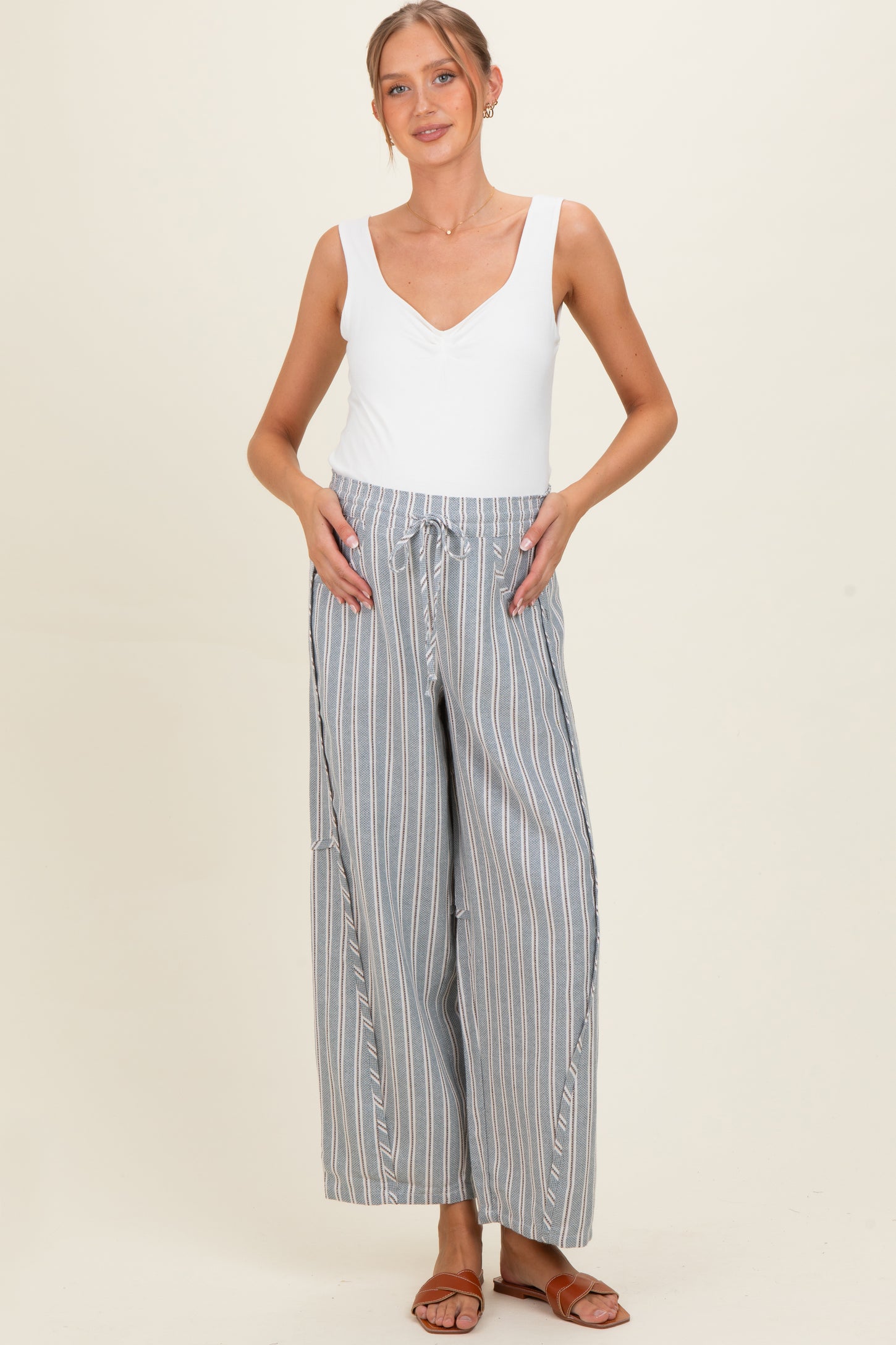 woman wearing a white sleeveless maternity top and striped wide-leg maternity pants with side pockets