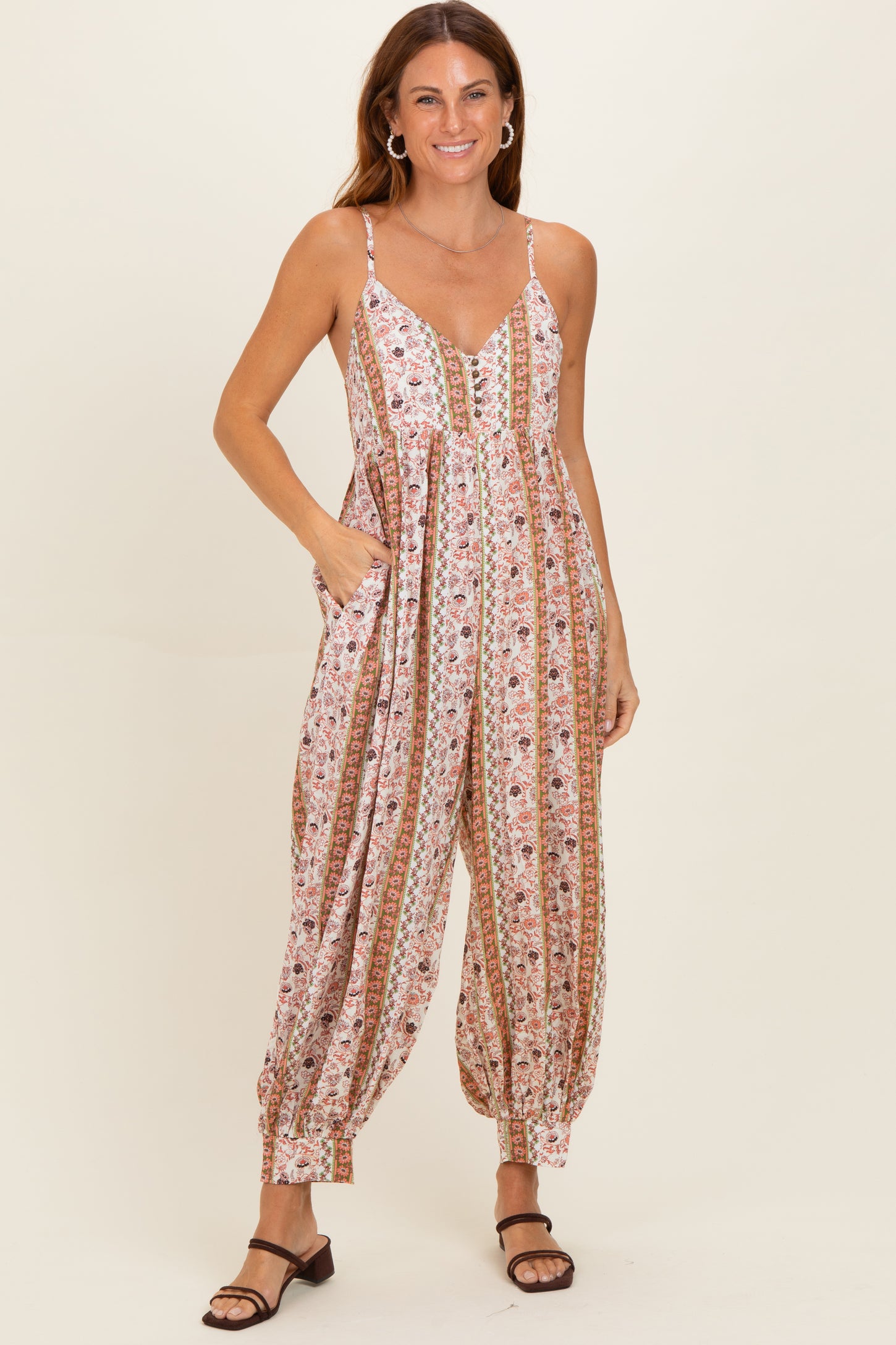 woman wearing a floral print sleeveless jumpsuit with pockets and comfortable fit, styled with brown sandals