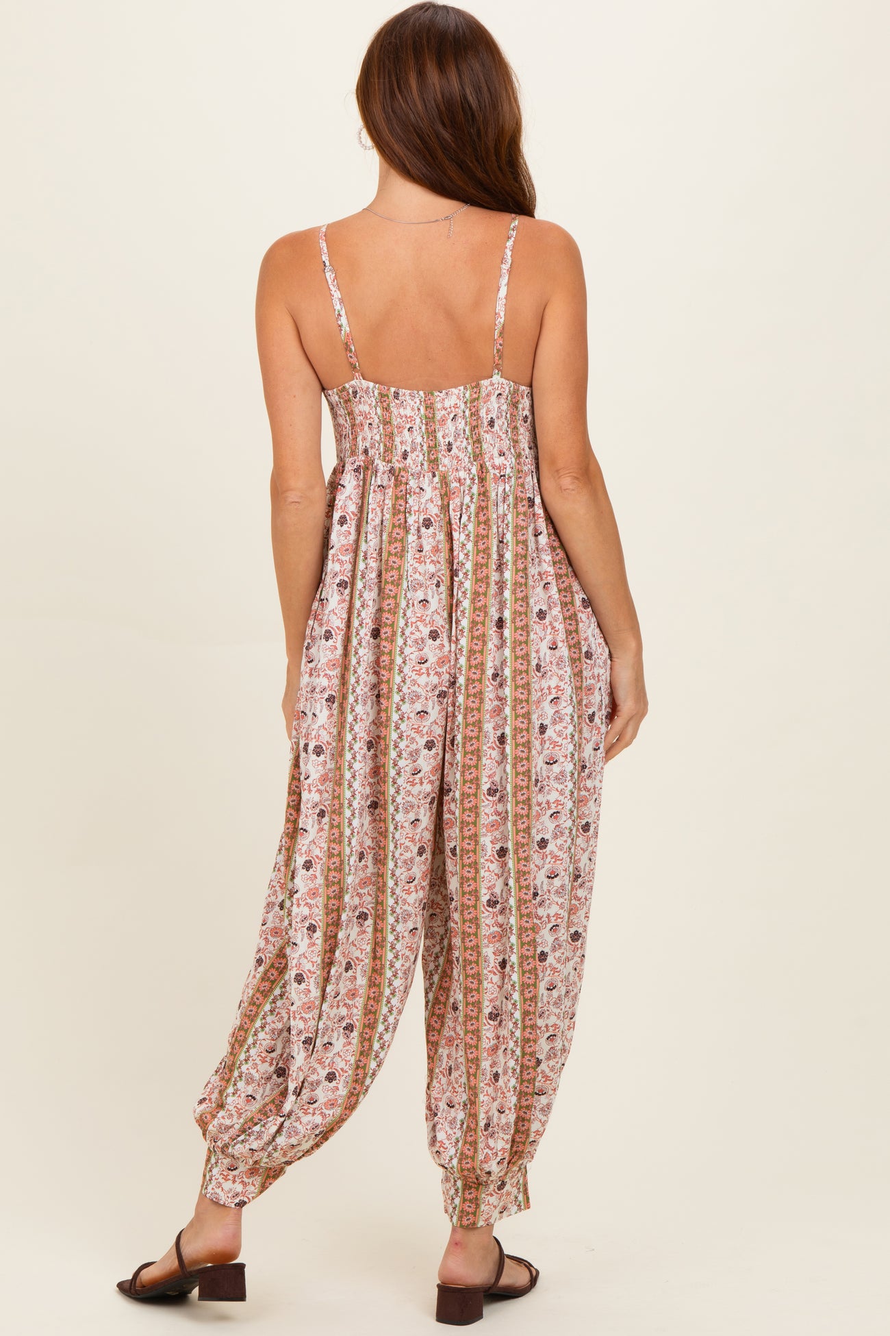woman wearing a pink floral patterned jumpsuit with adjustable straps and harem-style pants