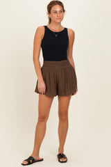 woman wearing a black sleeveless top and brown high-waisted shorts, standing with one hand on her hip