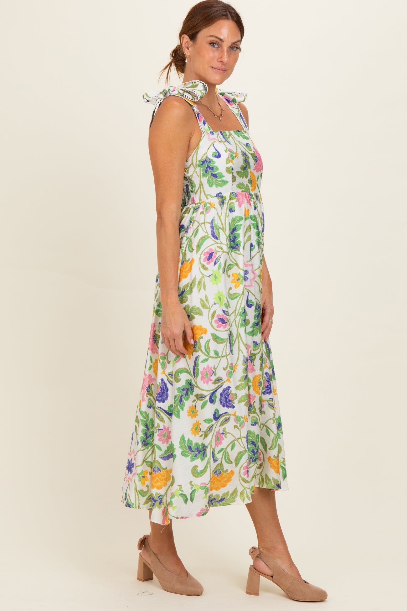 woman wearing a floral print midi dress with tie straps and a smocked bodice, paired with beige heels