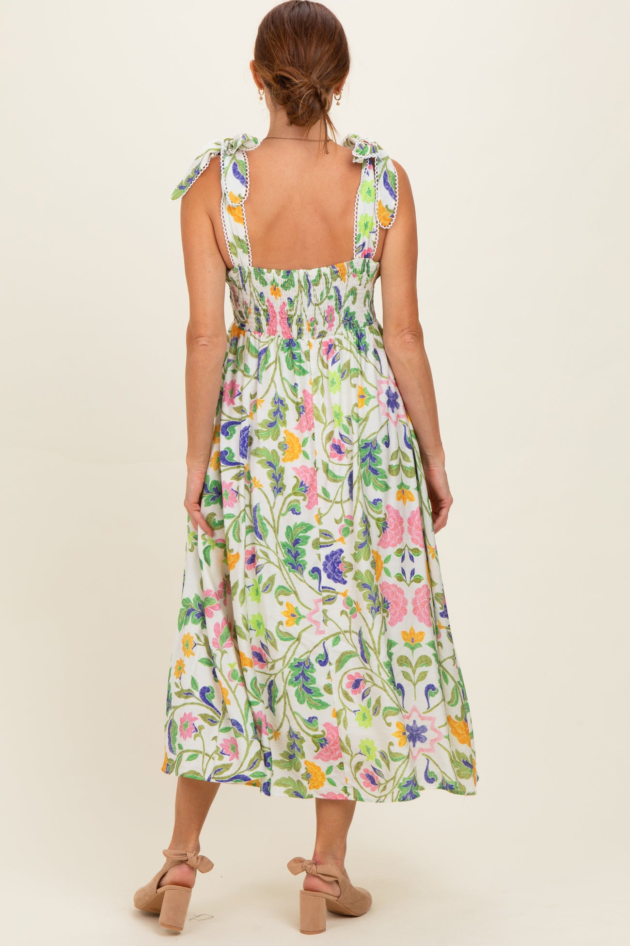 woman wearing a floral maxi dress with tie straps and smocked back, showcasing a vibrant green pattern with colorful flowers