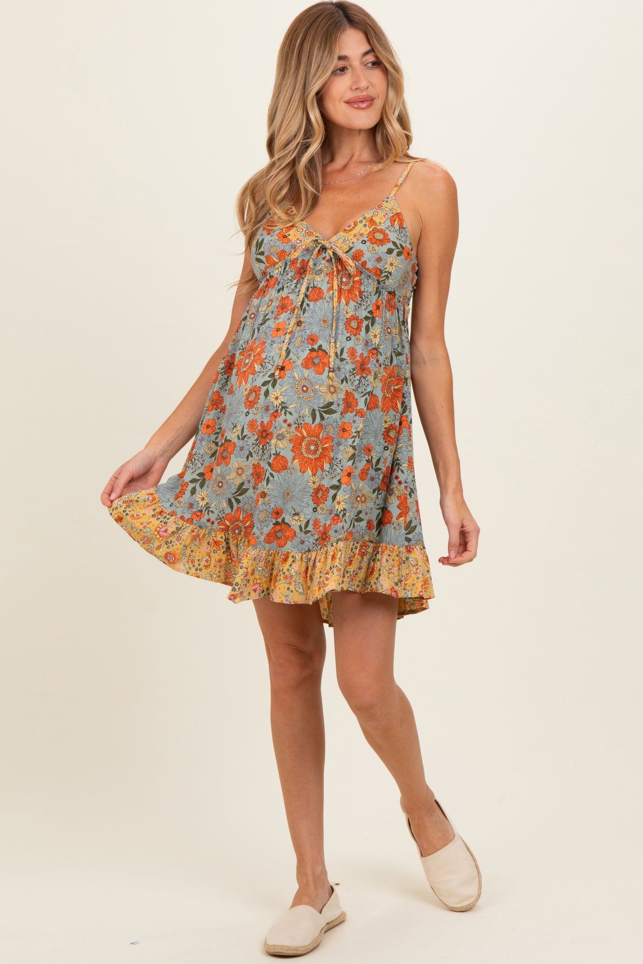 woman wearing a floral print maternity dress with spaghetti straps and a ruffle hem, holding the skirt out slightly