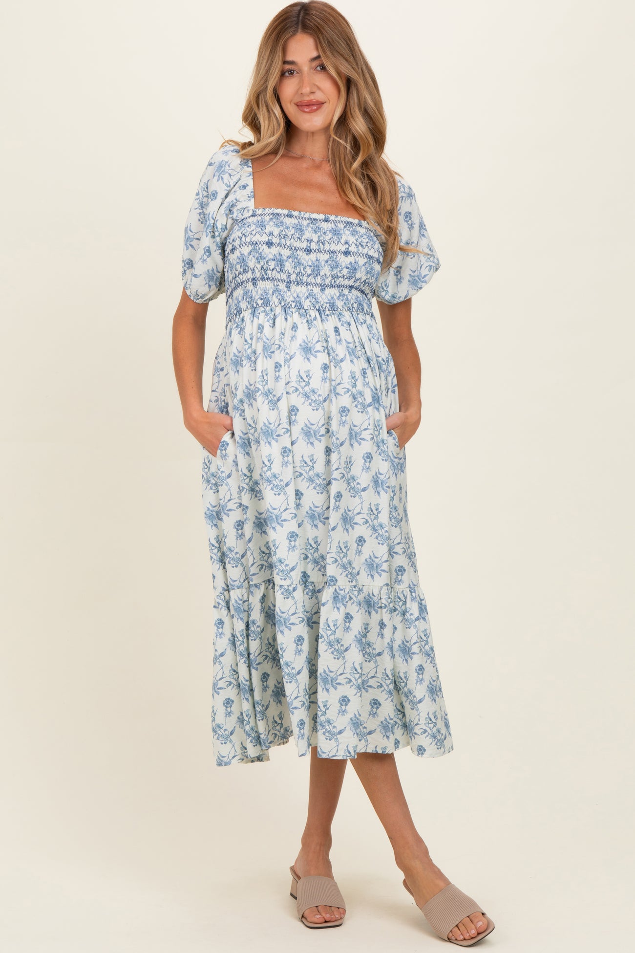 woman wearing a blue and white floral maternity dress with a smocked bodice and puff sleeves, holding her baby bump