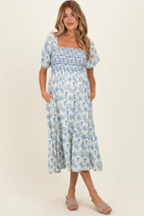 woman wearing a blue and white floral maternity dress with a smocked bodice and puff sleeves, holding her baby bump