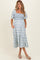 woman wearing a blue and white floral maternity dress with a smocked bodice and puff sleeves, holding her baby bump