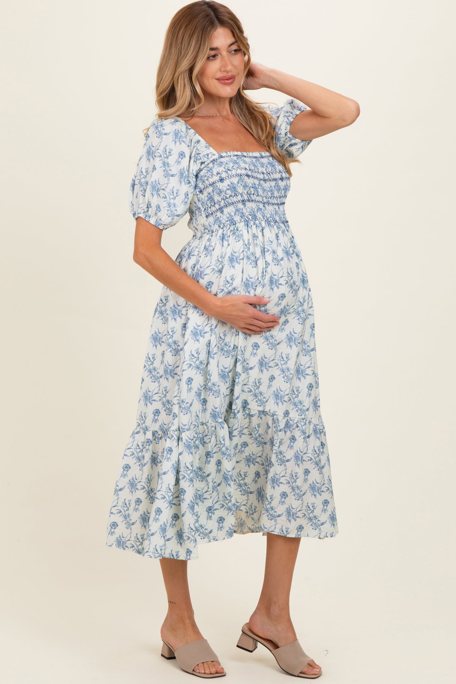 woman wearing a blue floral maternity dress with puff sleeves and a smocked bodice, holding her baby bump