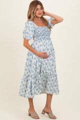 woman wearing a blue floral maternity dress with puff sleeves and a smocked bodice, holding her baby bump