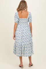 woman wearing a blue floral maternity dress with puff sleeves and a smocked back, showing off her baby bump