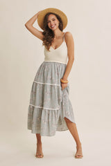 woman wearing a cream knitted tank top and floral tiered midi skirt, smiling and holding a straw hat