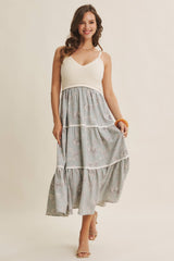 woman wearing a light grey floral maxi dress with a white bodice and tiered skirt, smiling and holding an orange