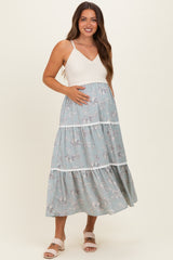 woman wearing a maternity maxi dress with a white knitted bodice and a blue floral tiered skirt, holding her baby bump