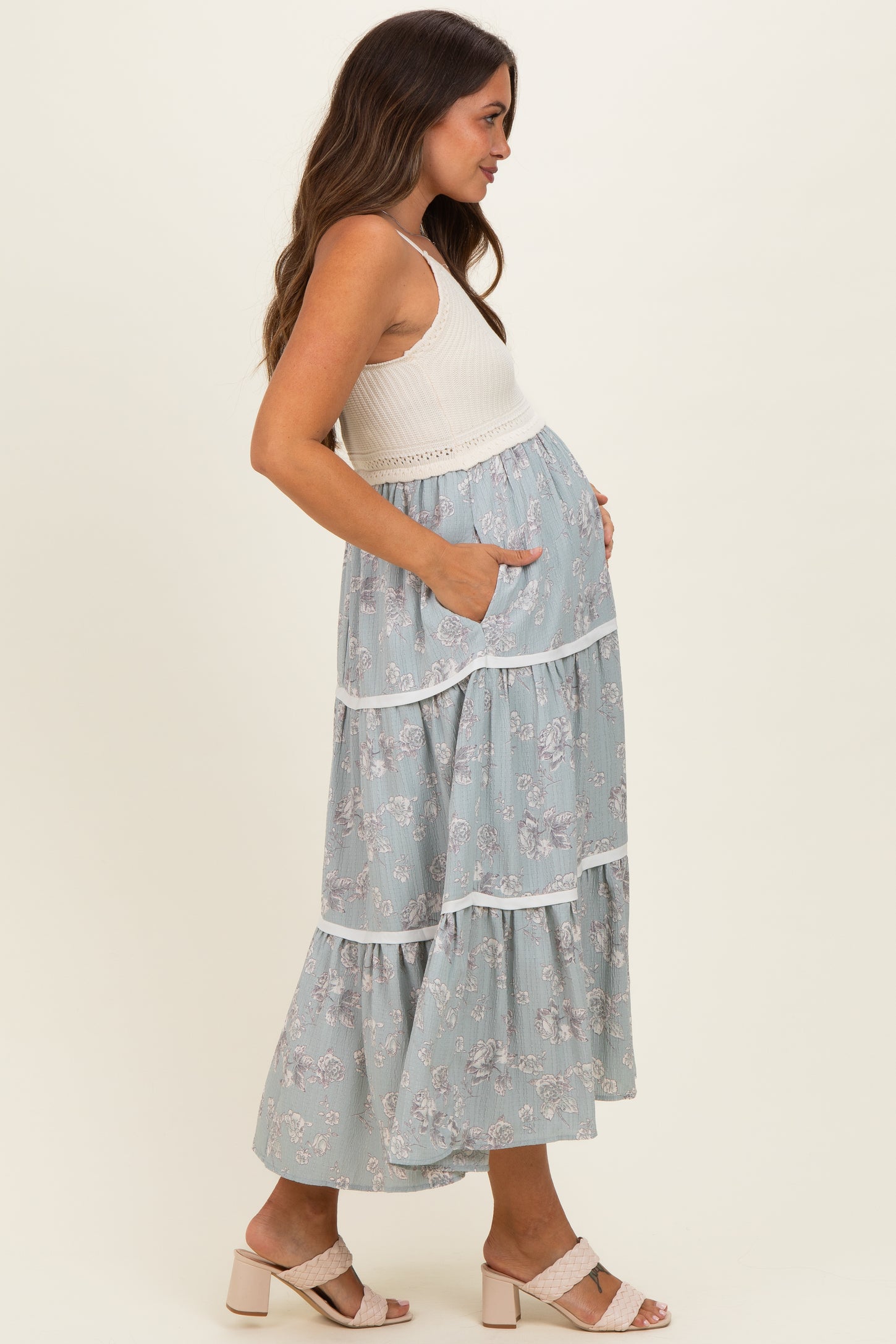 woman wearing a light blue floral maternity dress with tiered ruffles and pockets, showcasing her baby bump
