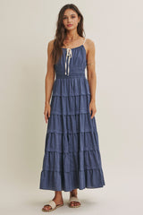 woman wearing a denim tiered maxi dress with spaghetti straps and a tie detail at the neckline
