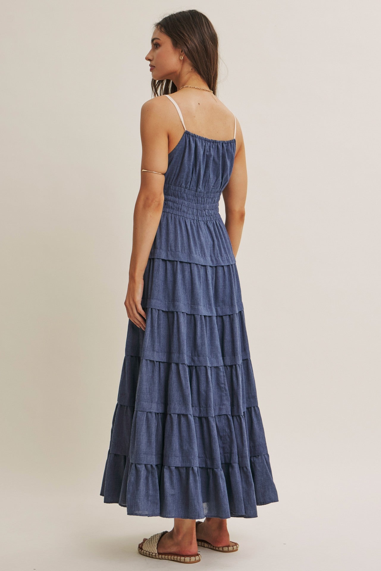 woman wearing a tiered denim maxi dress with a smocked bodice and spaghetti straps, viewed from the back