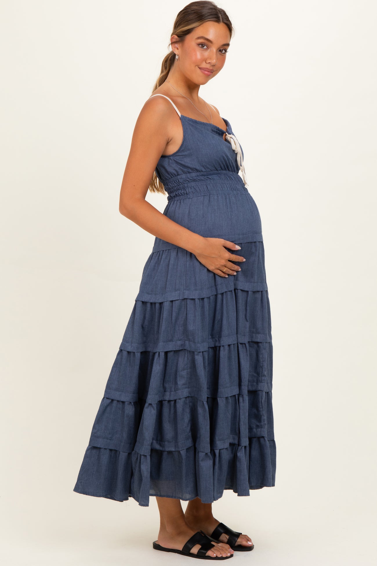 woman wearing a navy blue tiered maternity dress with adjustable straps and holding her baby bump