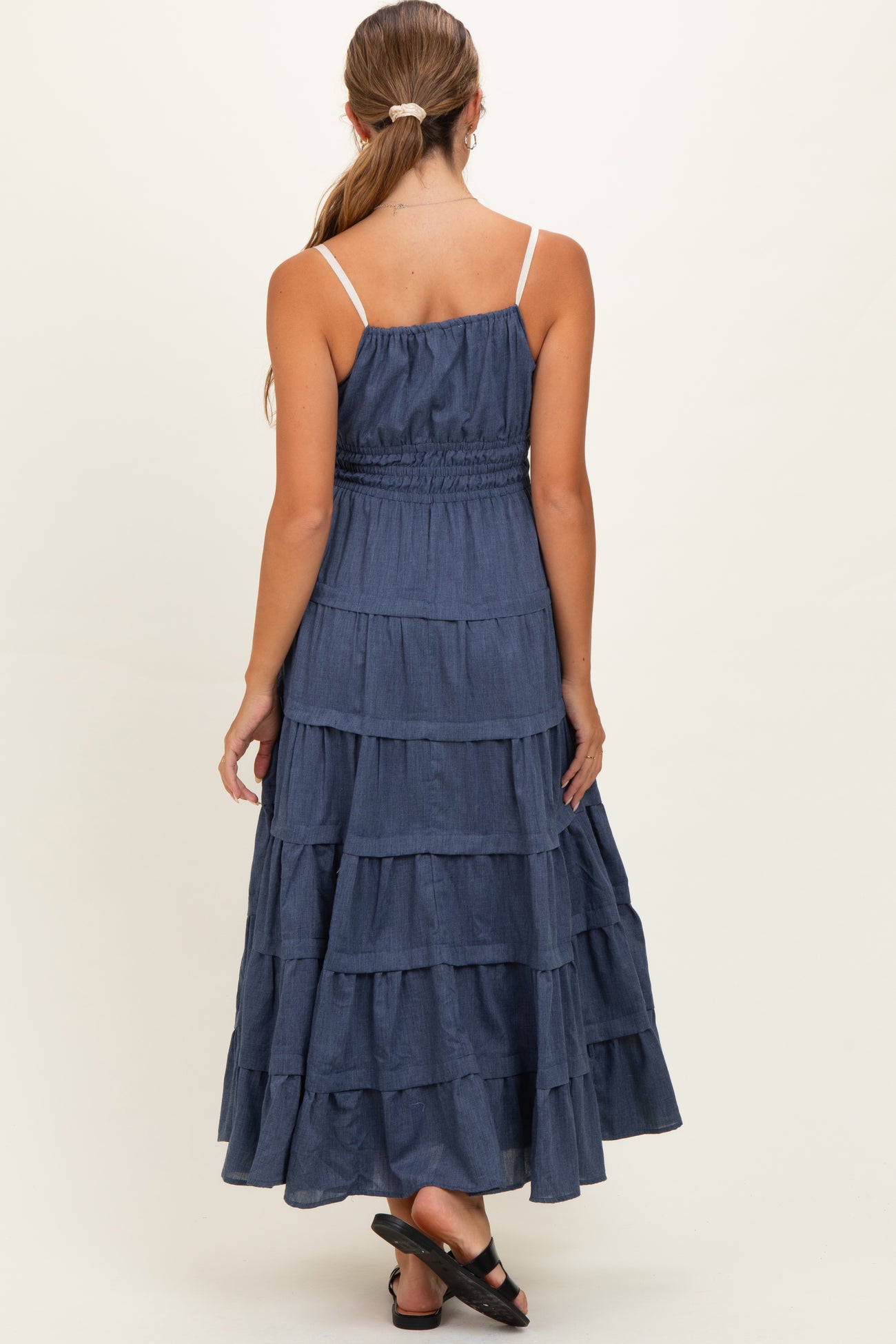 woman wearing a navy blue tiered maternity maxi dress with adjustable spaghetti straps and smocked bodice, full back view