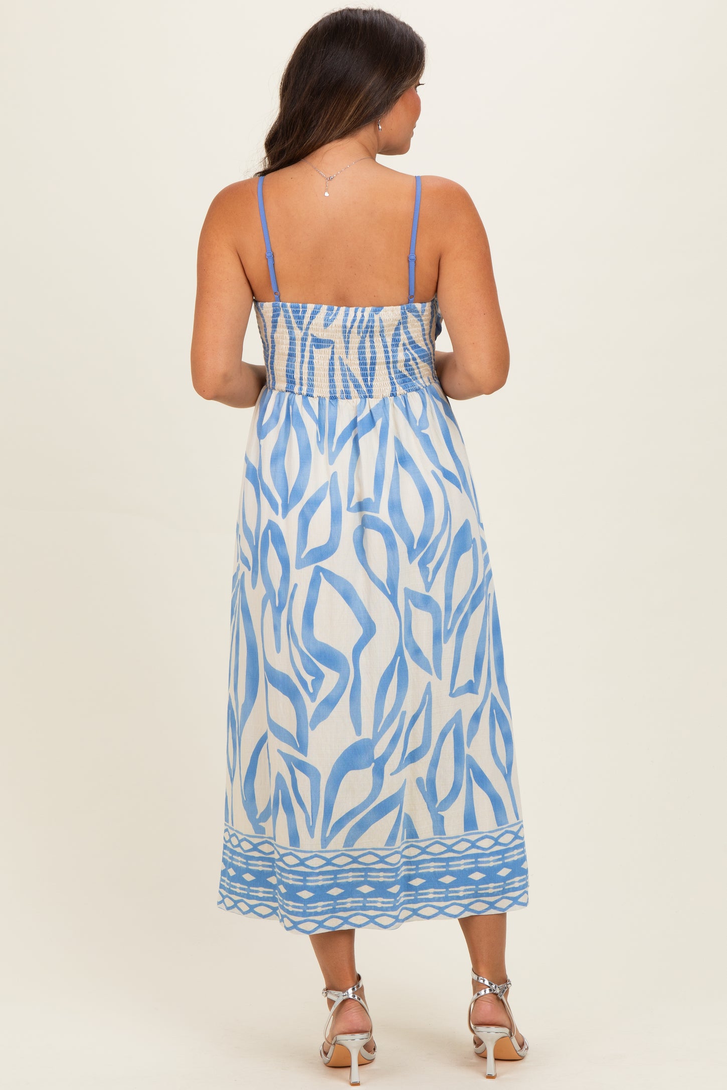 woman wearing a blue and white patterned maternity maxi dress with smocked bodice and spaghetti straps, showing her baby bump