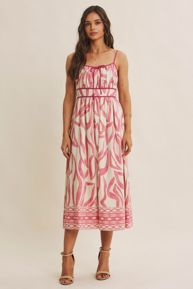 woman wearing a midi dress with a pink and white abstract print and spaghetti straps, standing against a neutral background