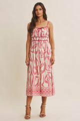 woman wearing a midi dress with a pink and white abstract print and spaghetti straps, standing against a neutral background