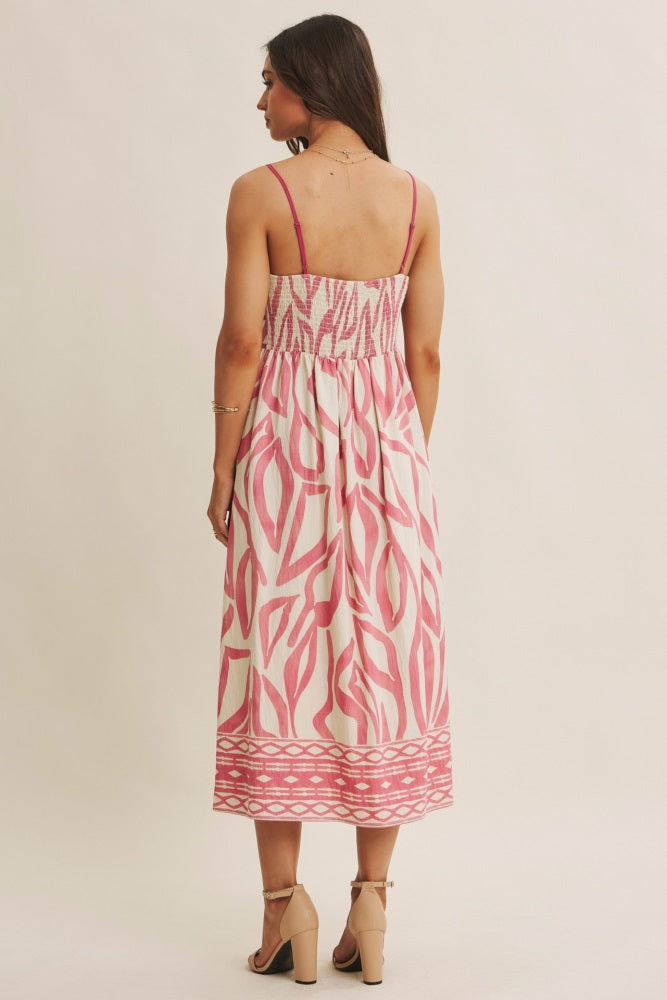 woman wearing a back view of a pink and white patterned midi dress with spaghetti straps and smocked bodice