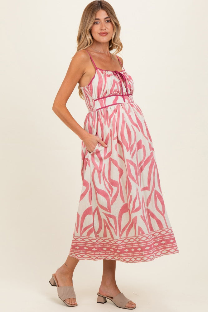 woman wearing a pink and white patterned maternity dress with a fitted bodice and pockets, showing her baby bump