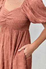 woman wearing a terracotta smocked midi dress with puff sleeves and side pockets