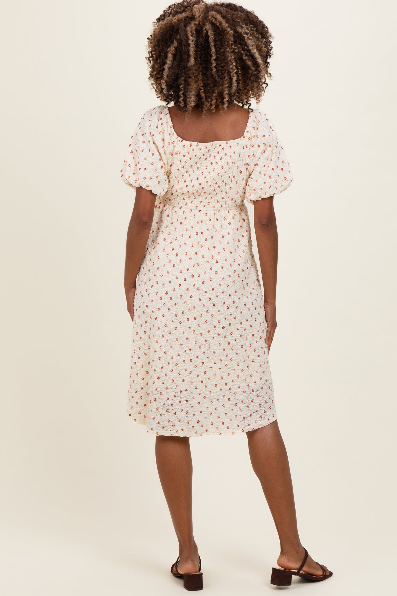 woman wearing a white short sleeve maternity dress with a floral print and gathered back detail