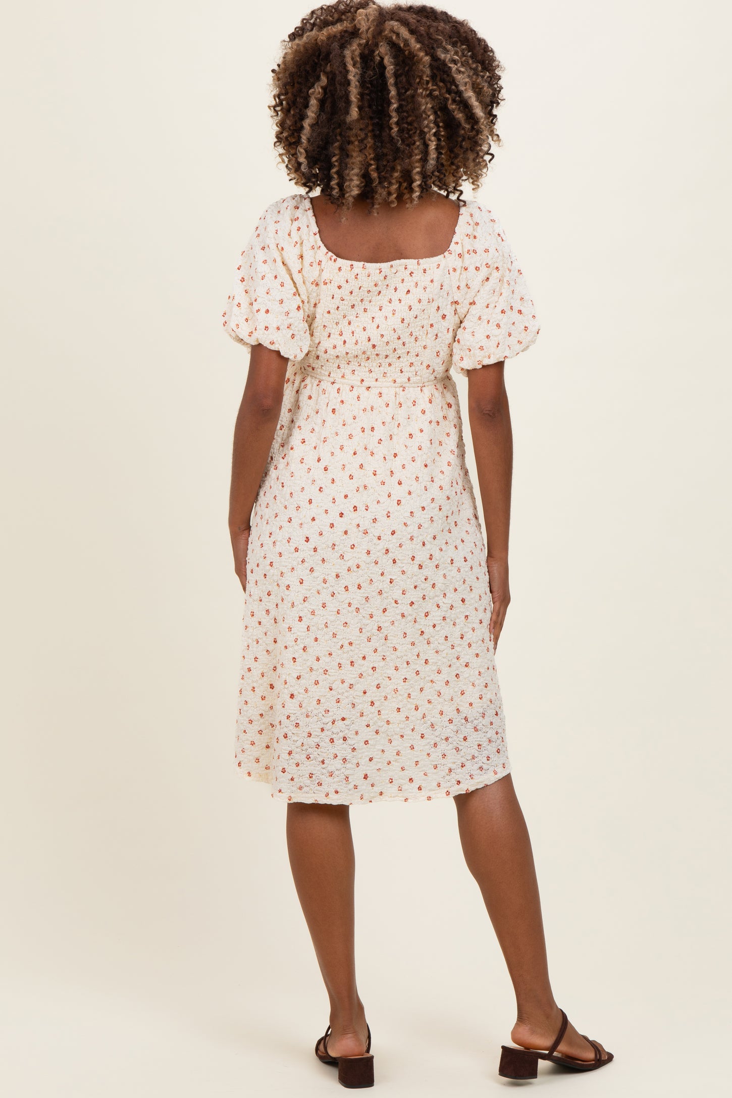 woman wearing a white short sleeve maternity dress with a floral print and gathered back detail