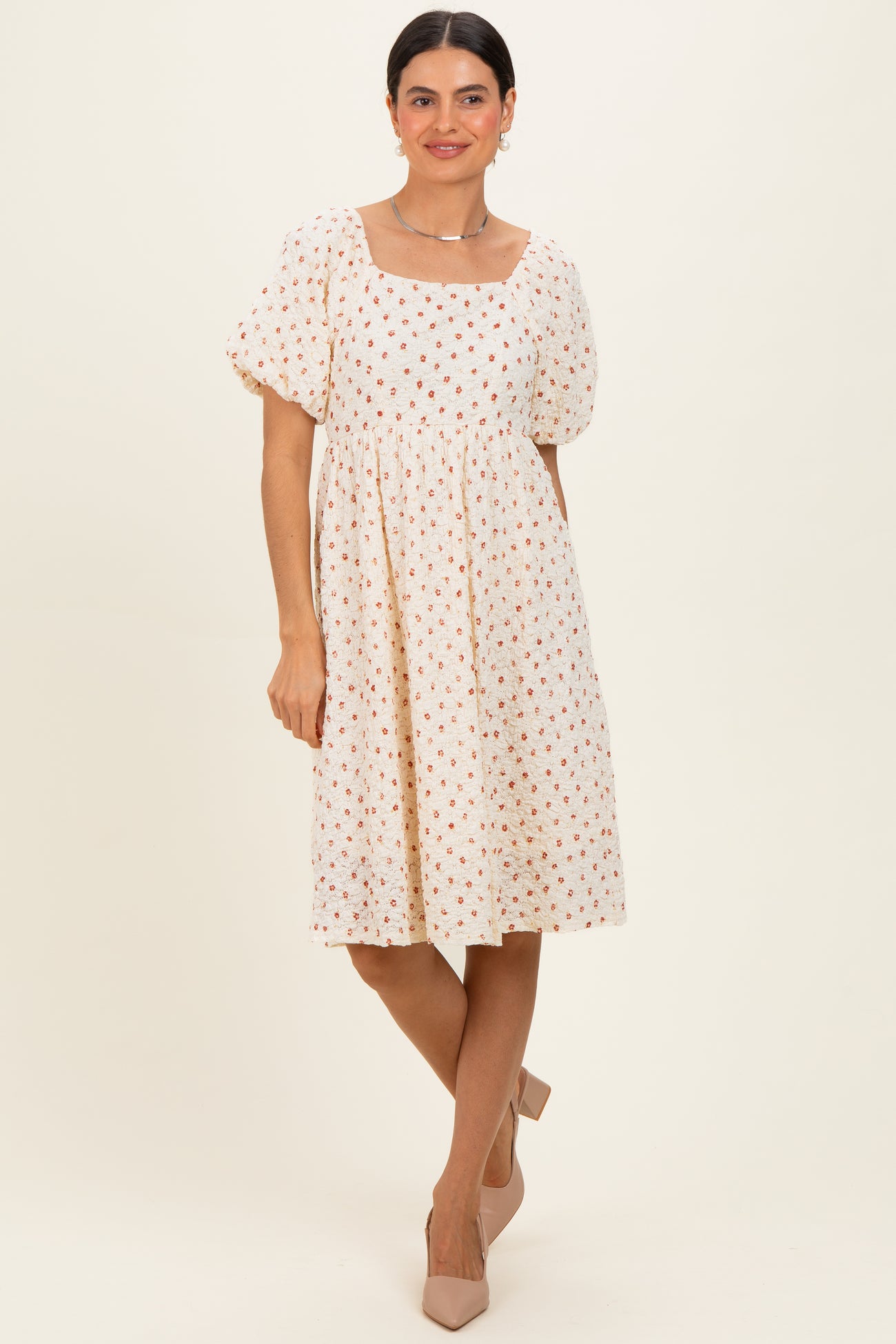 woman wearing a cream floral puff sleeve dress with a square neckline and knee-length hem