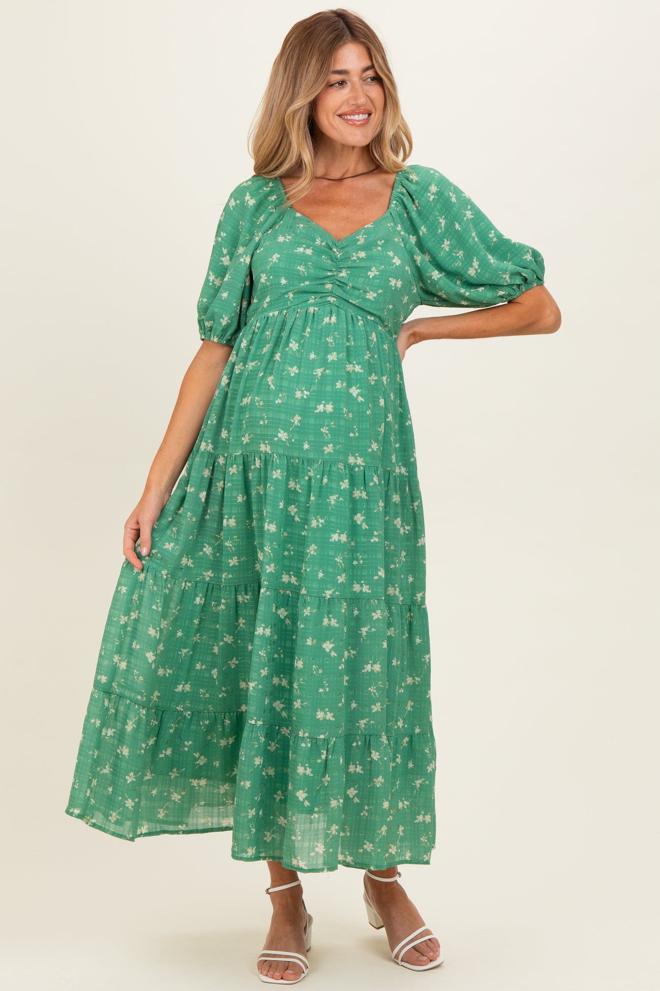 woman wearing a green floral maternity maxi dress with puff sleeves and a cinched Empire waist showcasing her baby bump