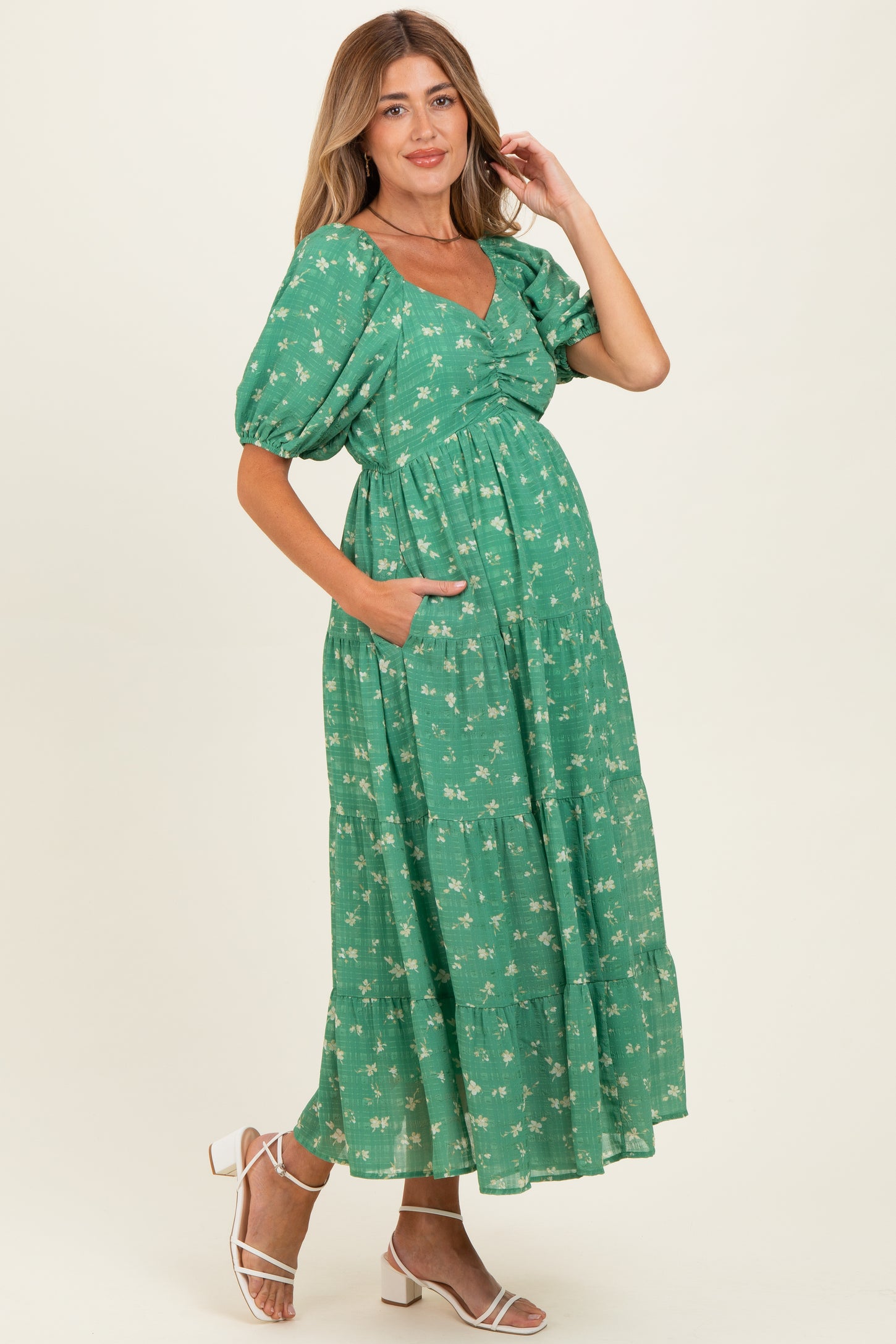 woman wearing a green floral maternity dress with puff sleeves and pockets, showcasing her baby bump