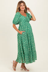 woman wearing a green floral maternity dress with puff sleeves and pockets, showcasing her baby bump