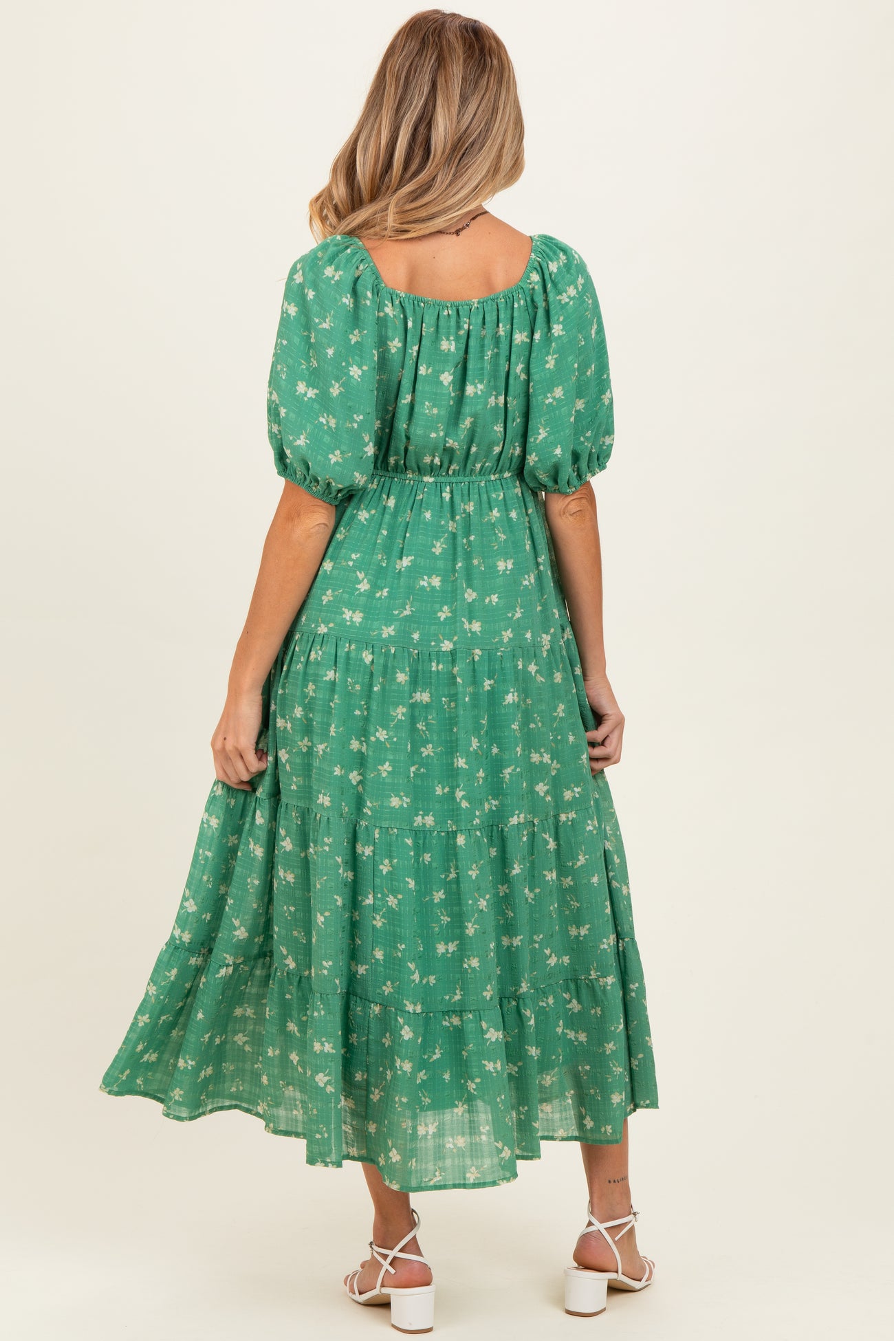 woman wearing a green floral maternity maxi dress with puff sleeves and a tiered skirt, showing off her baby bump