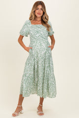 woman wearing a green floral midi maternity dress with puff sleeves and pockets, standing against a neutral background