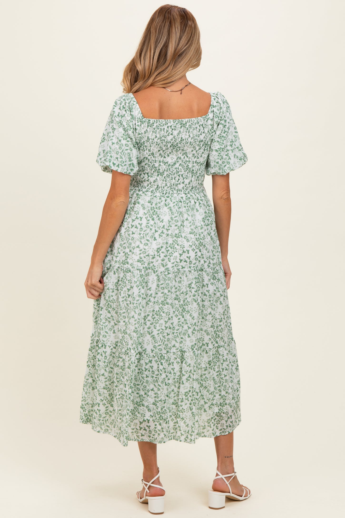 woman wearing a green floral maternity dress with puff sleeves and a smocked bodice, showing a flowy midi length