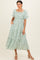woman wearing a white floral maxi dress with puff sleeves and square neckline, standing with hands in pockets