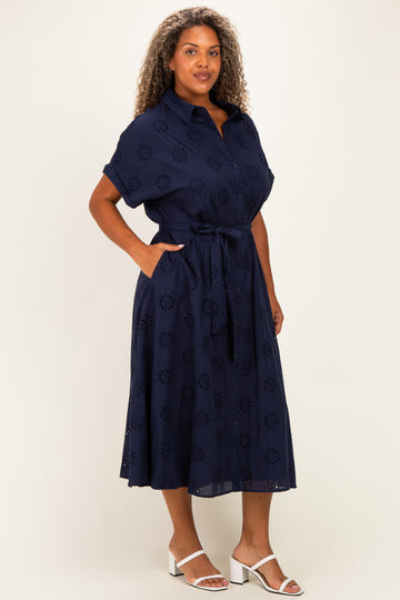 woman wearing a navy blue plus size dress with short sleeves, a tie belt, and floral embroidery details