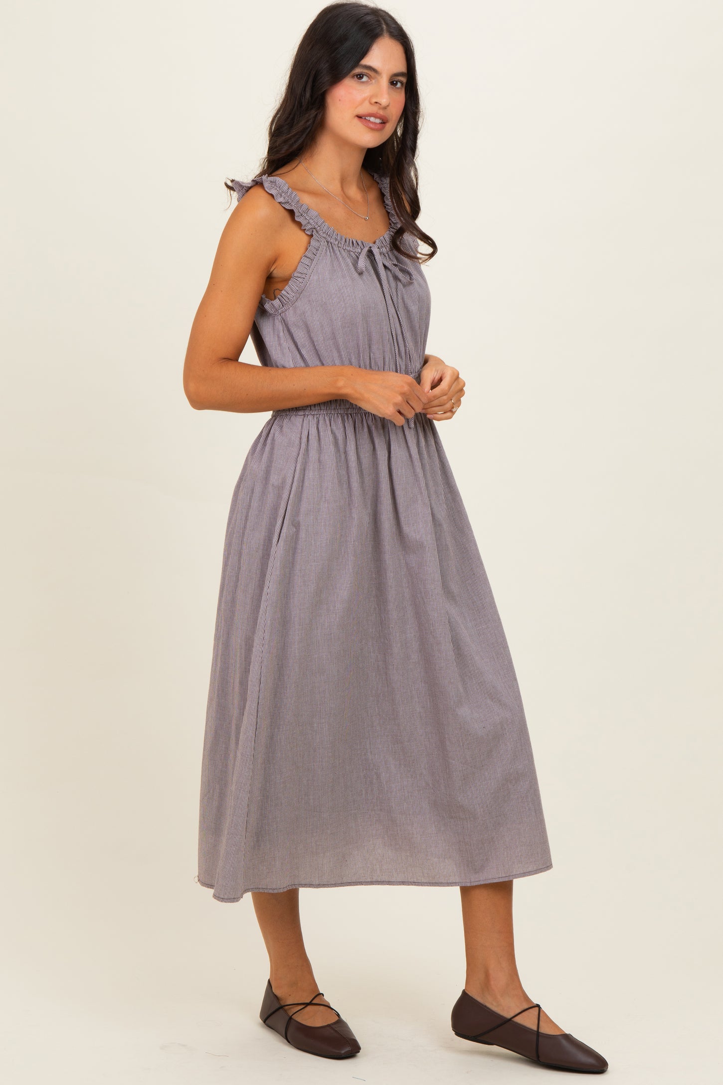 woman wearing a sleeveless gray and white striped midi dress with ruffle details and a tie at the neckline