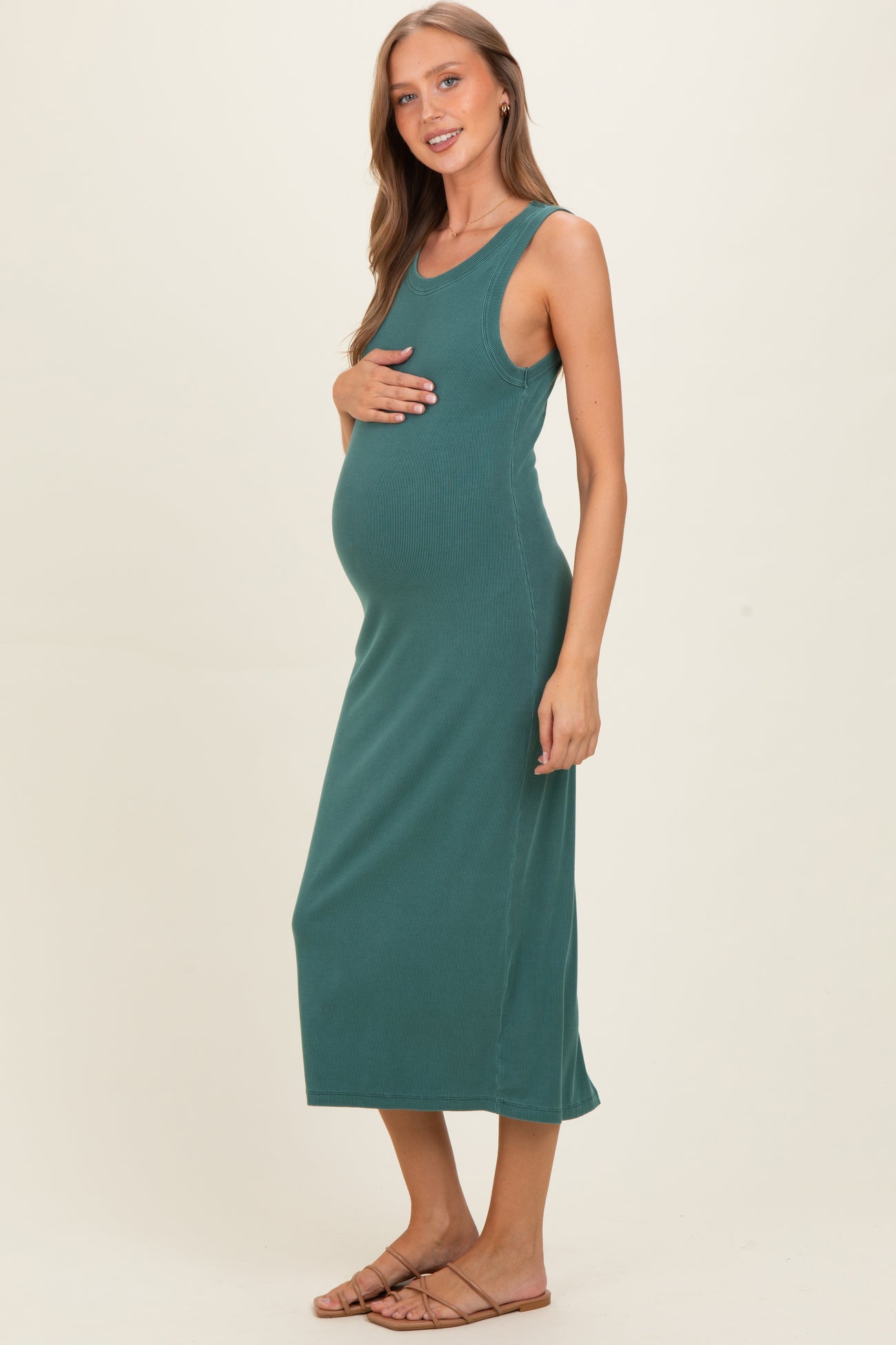 woman wearing a teal sleeveless maternity dress and holding her baby bump