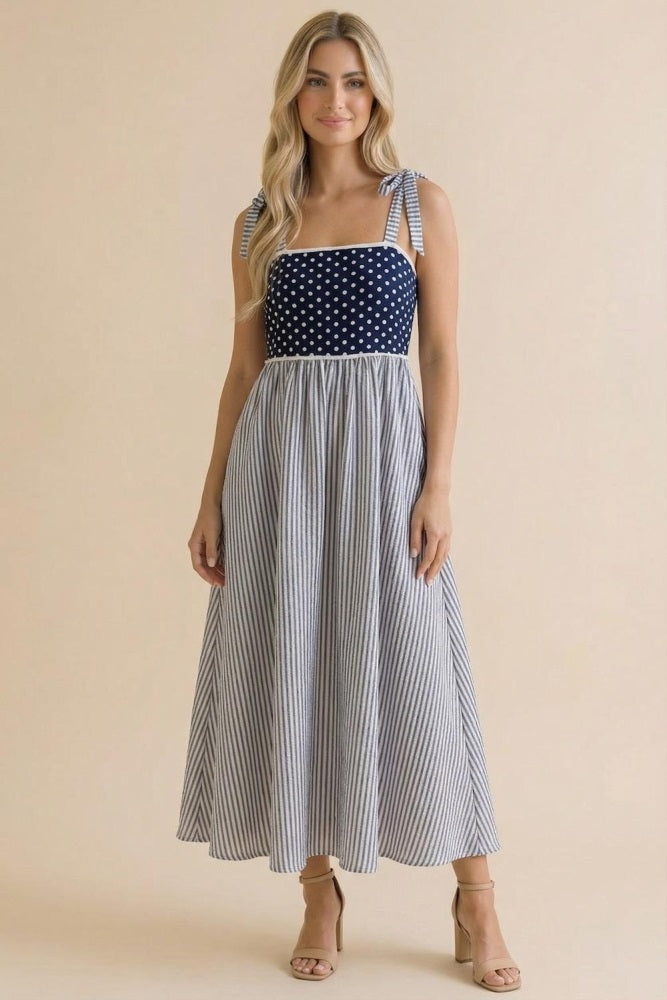 woman wearing a navy and white polka dot tie strap maxi dress with a striped skirt