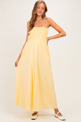 woman wearing a yellow smock style maternity maxi dress with adjustable straps and a relaxed fit
