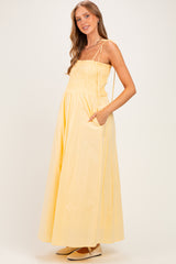 woman wearing a yellow maternity maxi dress with smocked bodice and pockets, showcasing her baby bump