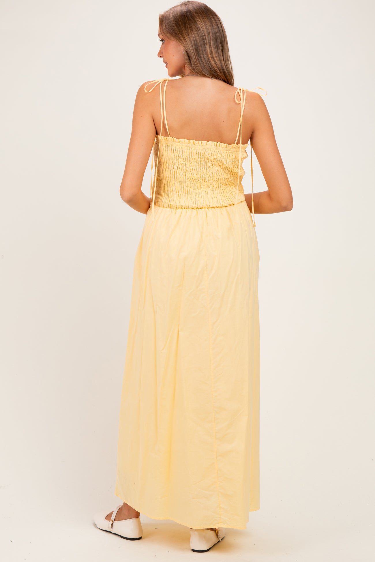 woman wearing a yellow maternity maxi dress with a smocked back and tie straps